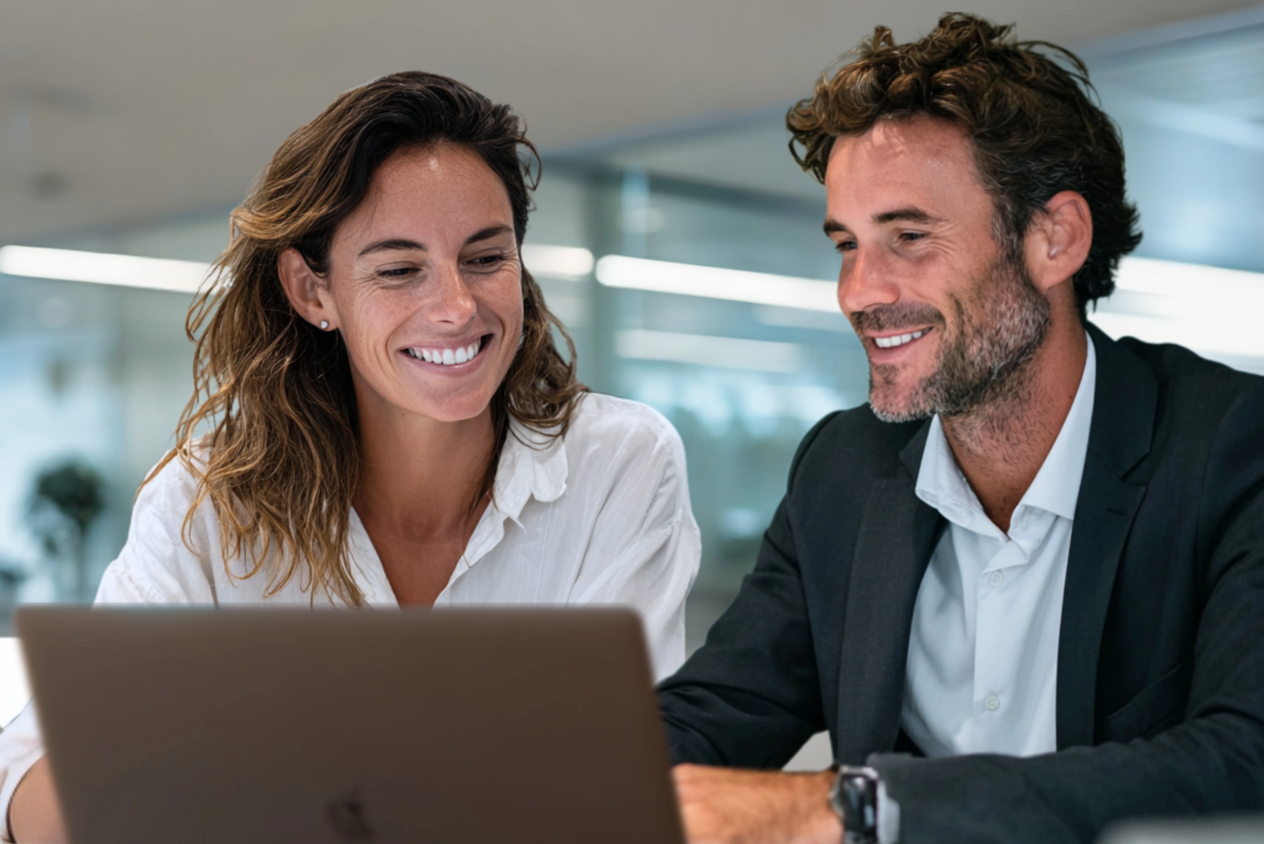 Two professionals collaborating and smiling while reviewing content on a laptop in an office.